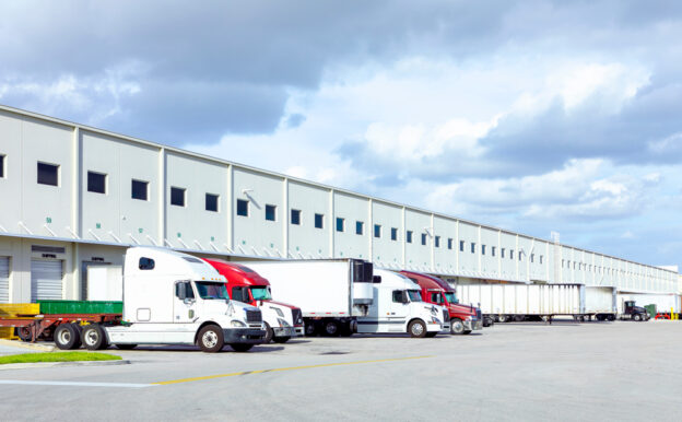 Freight forwarding trucks and trailers parked behind warehouses.