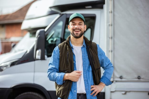 owner-operator truck driver standing in front of his truck smiling